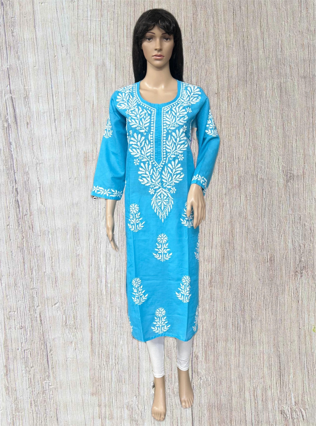 A bright blue three-quarter sleeve kurta with white floral embroidery, displayed on a female mannequin against a light wood-textured background.