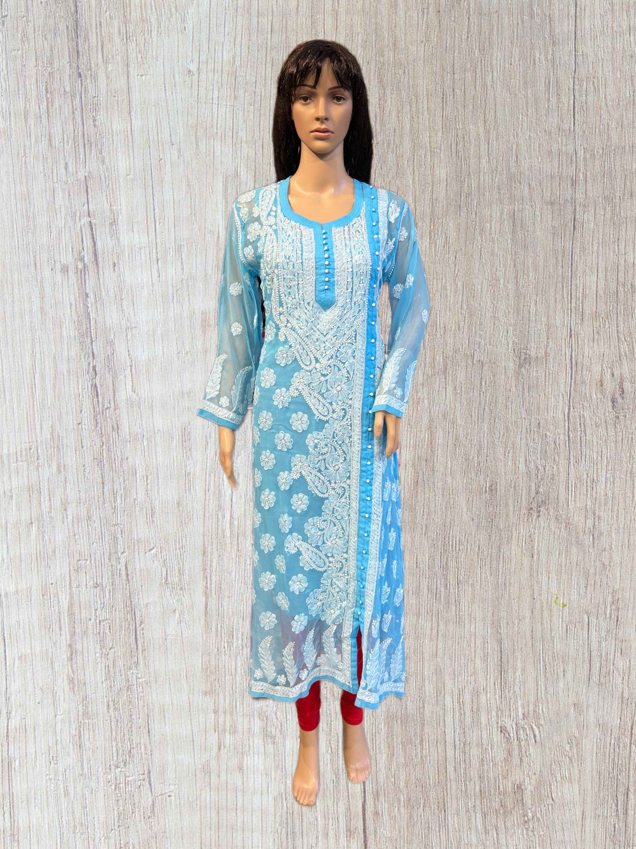 Light blue embroidered dress on a mannequin against a wooden panel background