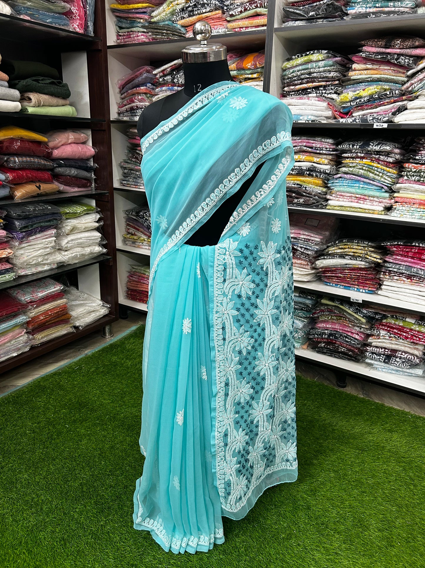 Light blue saree with white embroidery on a mannequin in a fabric store.