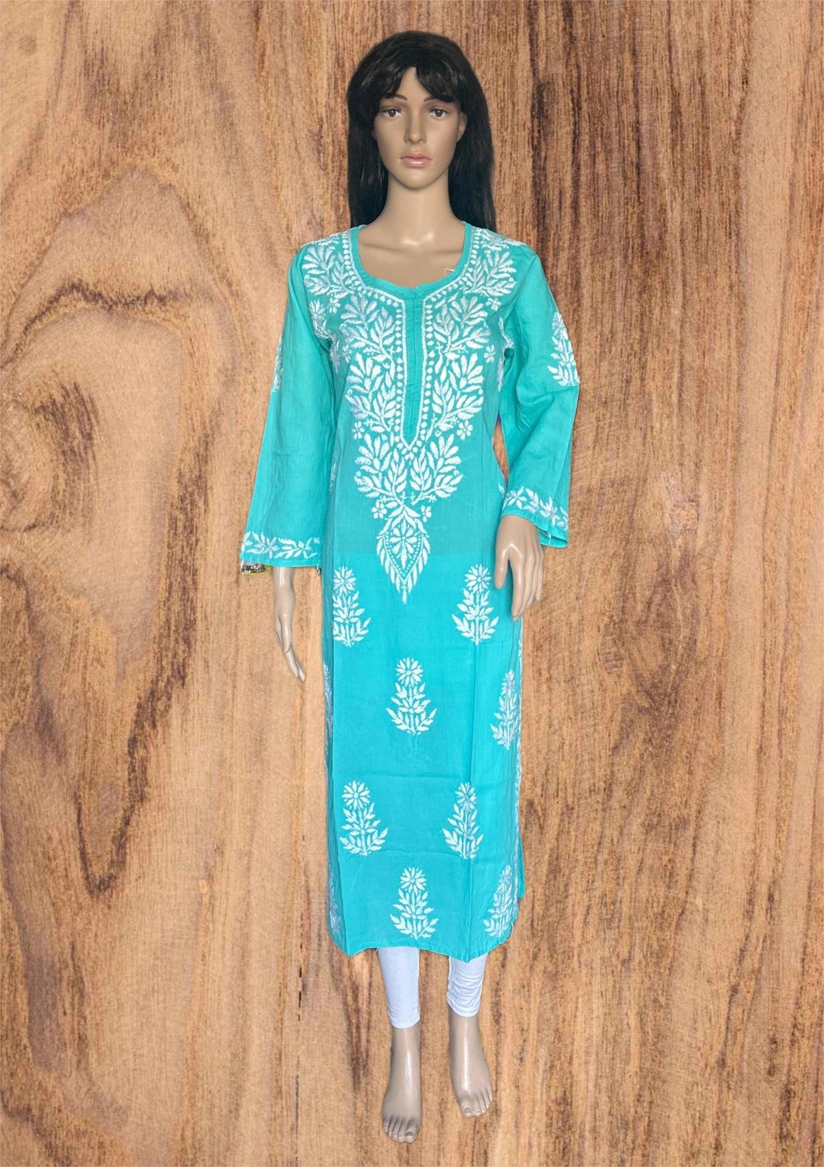 Green and white embroidered dress on a mannequin against a wooden background