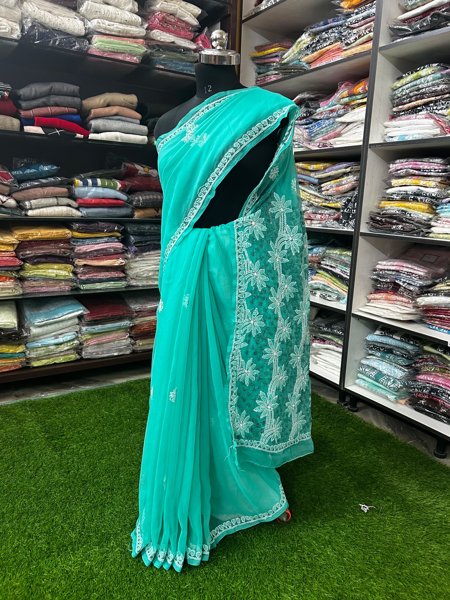 Turquoise saree with white embroidery on a mannequin in a fabric store.