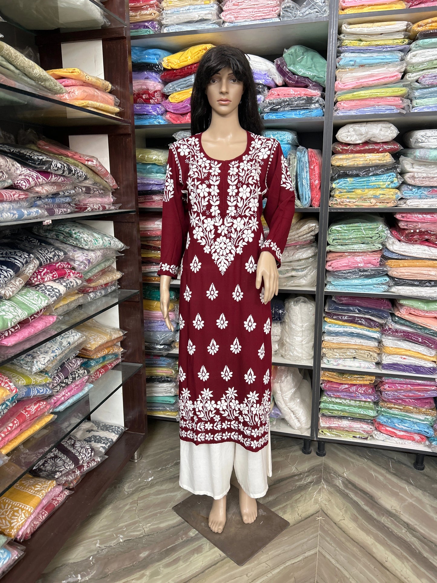 Lucknowi Chikankari Mannequin wearing a red and white dress in a fabric store with shelves of colorful fabrics.