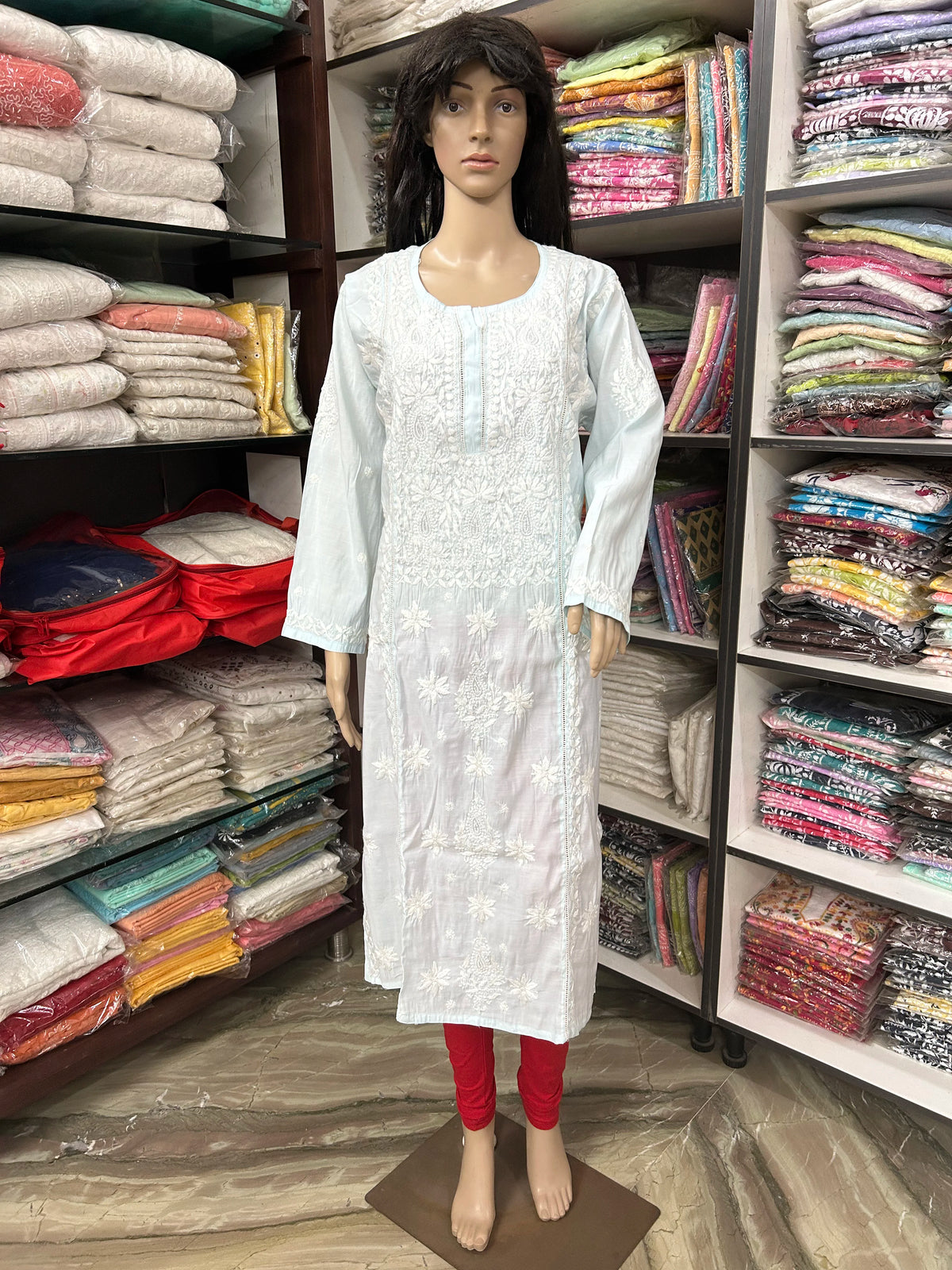 A white embroidered kurta with light blue sleeves and red leggings displayed on a female mannequin in a clothing store.