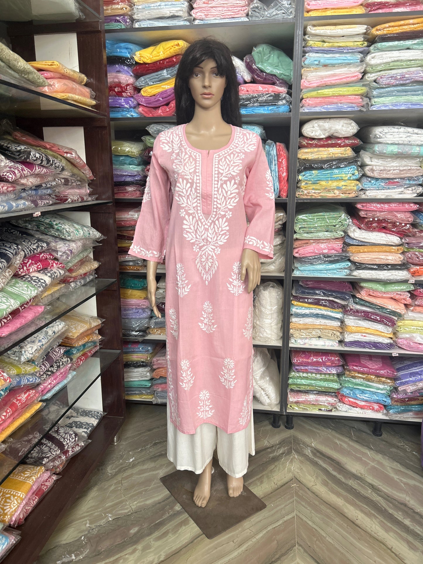 Mannequin wearing a pink embroidered kurta with white pants in a fabric store.