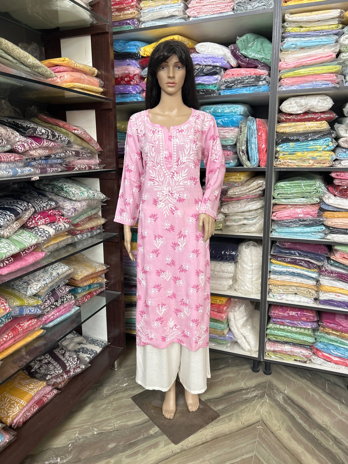 lucknowi chikankari Mannequin wearing a pink dress in a fabric store with shelves of colorful fabrics.