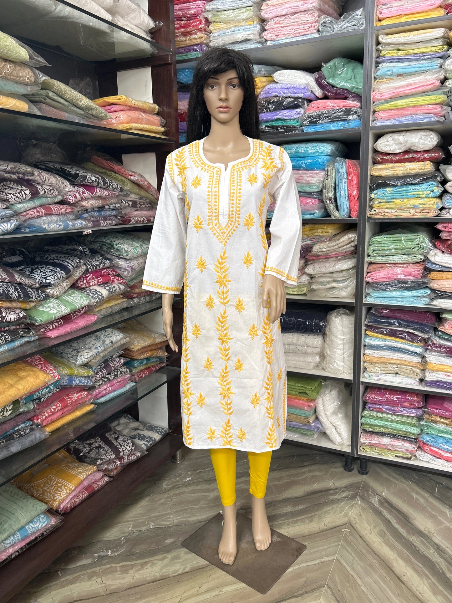 Mannequin wearing a white kurta with yellow embroidery in a fabric store.