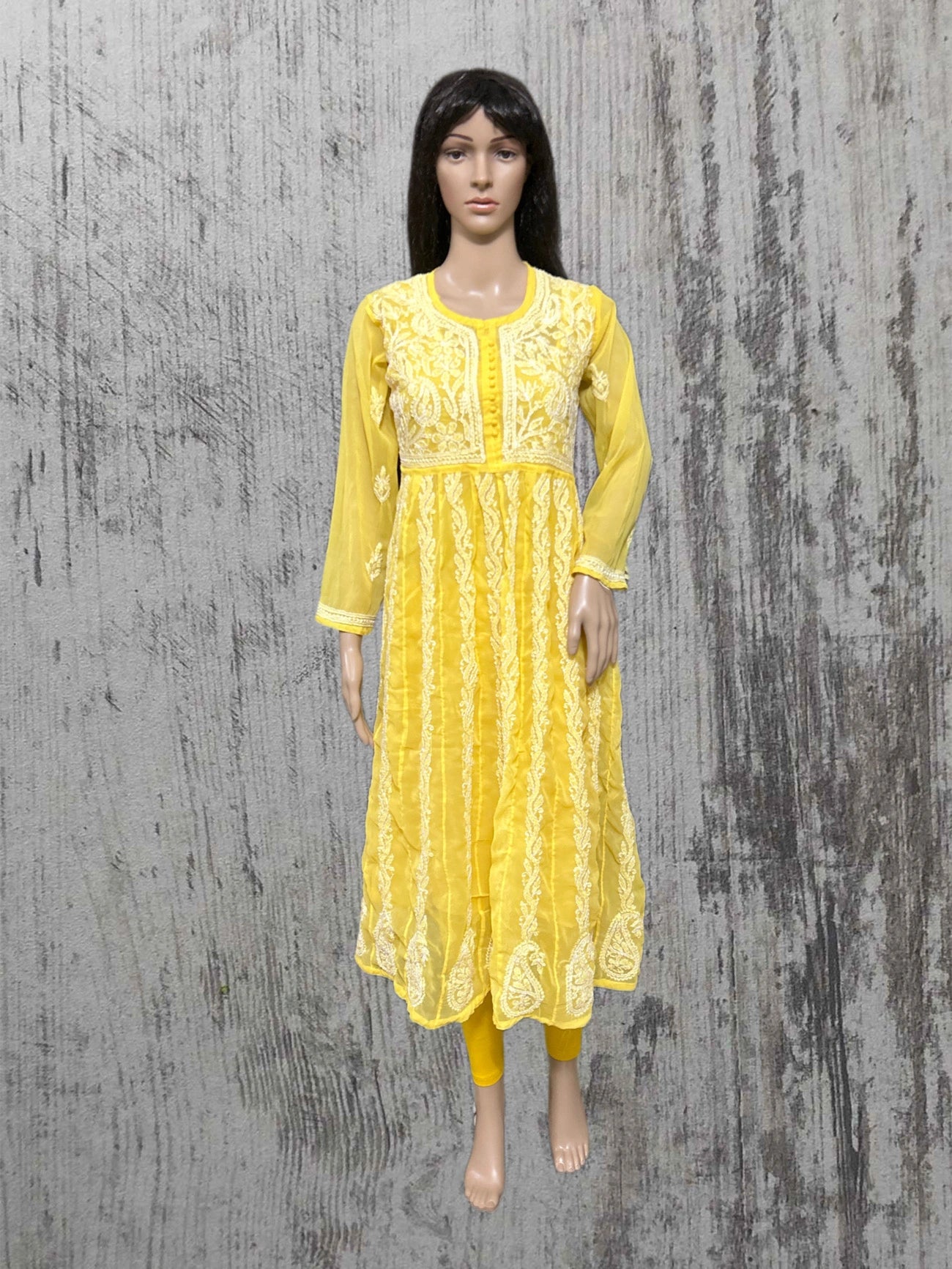 Yellow embroidered dress on a mannequin against a textured gray background