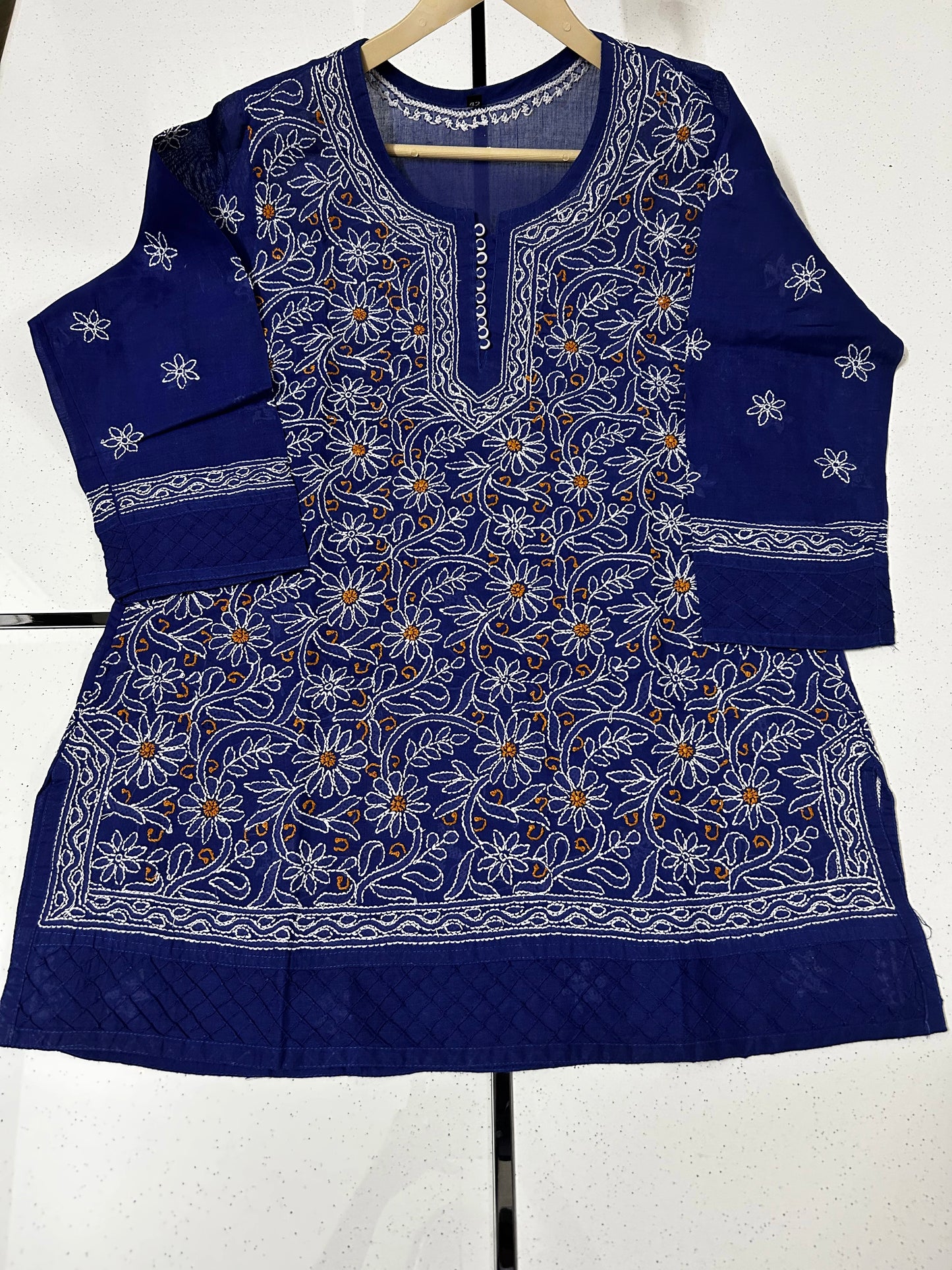 Blue embroidered traditional outfit on a hanger against a white background