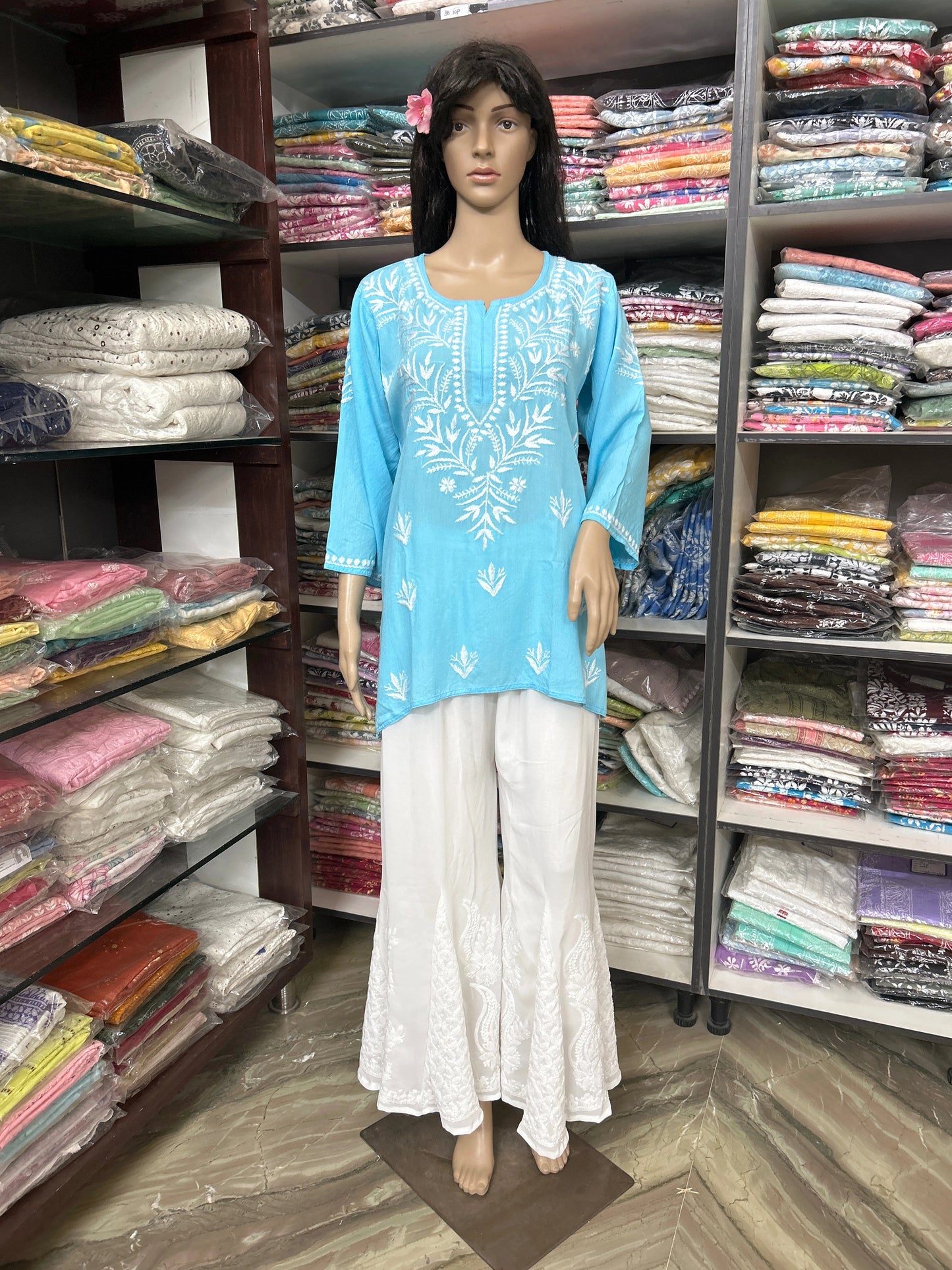 Mannequin wearing a blue embroidered top and white pants in a fabric store.