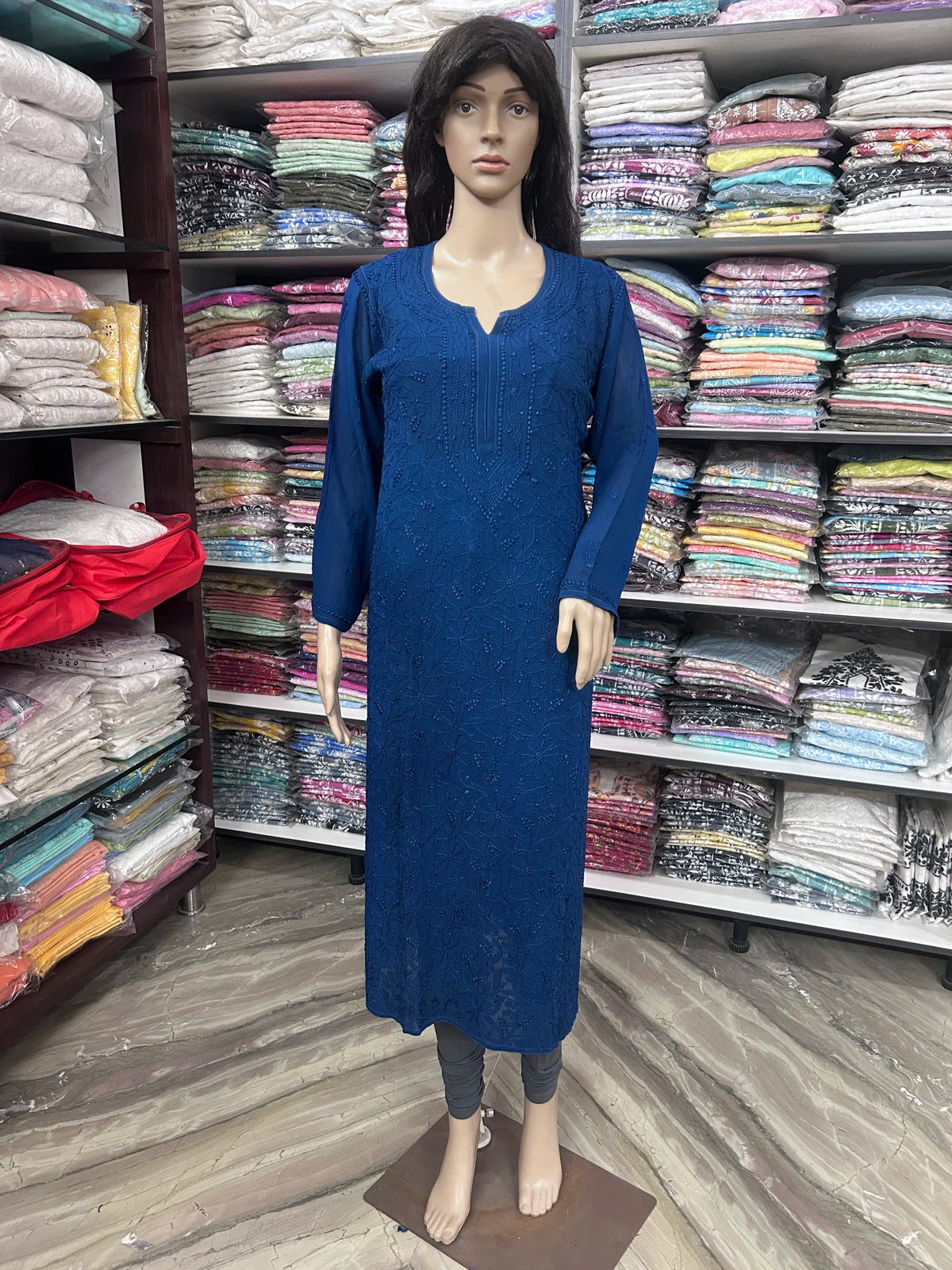 lucknowi chikankari A bright blue long-sleeve kurta displayed on a female mannequin inside a clothing store. The kurta features a split neckline and a subtle textured pattern, paired with dark gray leggings on the mannequin.