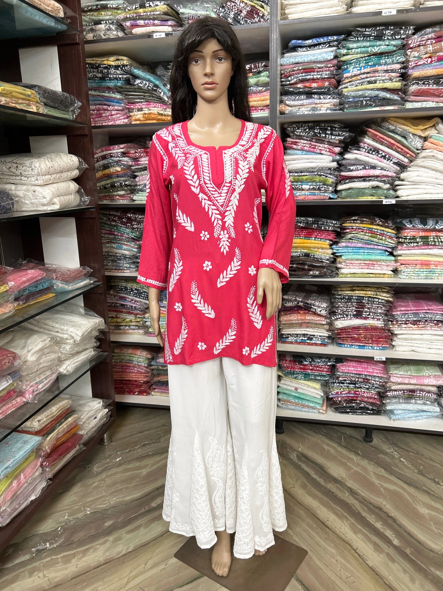 Mannequin wearing a lucknowi chikankari red and white embroidered top with white pants in a fabric store.