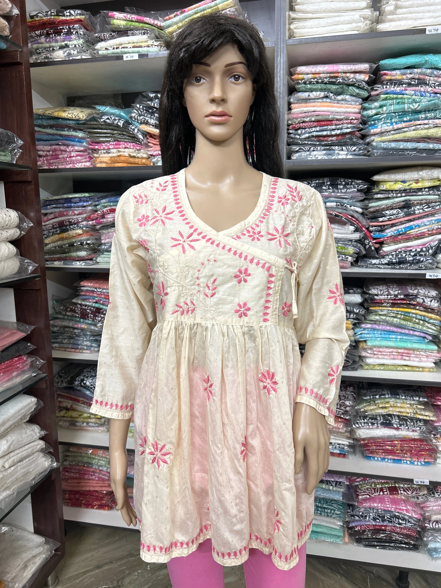 Mannequin wearing a cream-colored embroidered top in a fabric store.