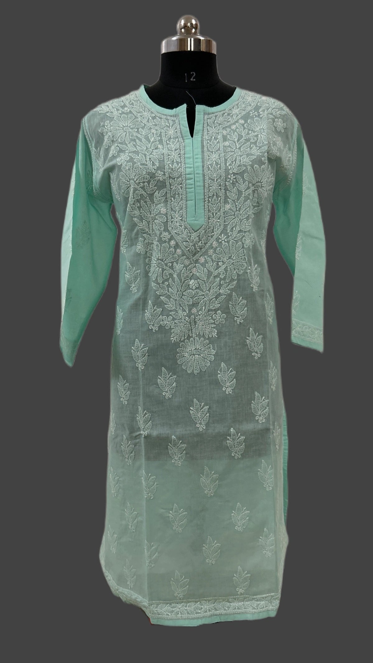 A mint green long-sleeve kurta with white floral embroidery, displayed on a black mannequin against a dark gray background.