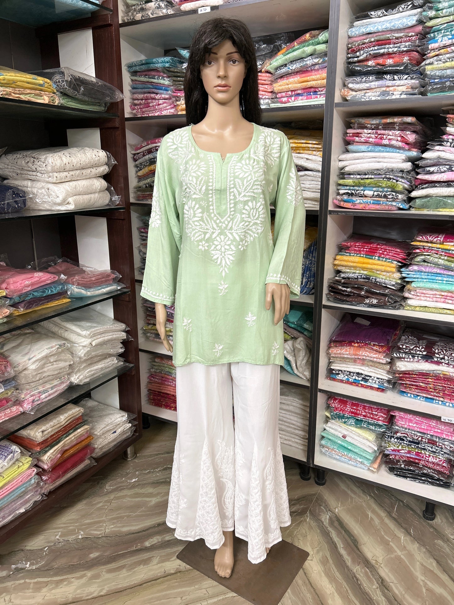 Mannequin wearing a lucknowi chikankari light green top and white pants in a fabric store.