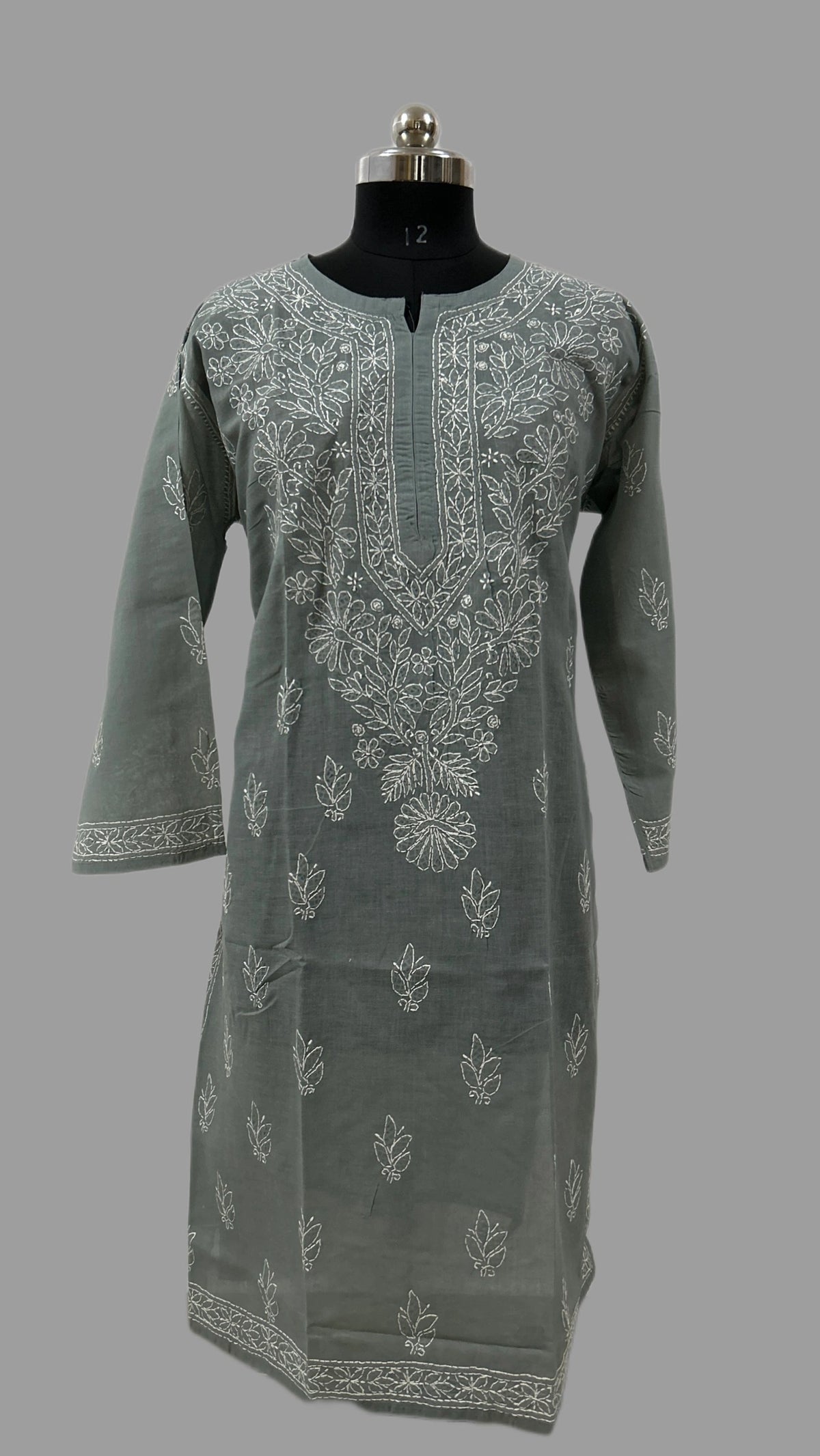 A sage green kurta with white floral embroidery, displayed on a black dress form mannequin against a solid gray background.