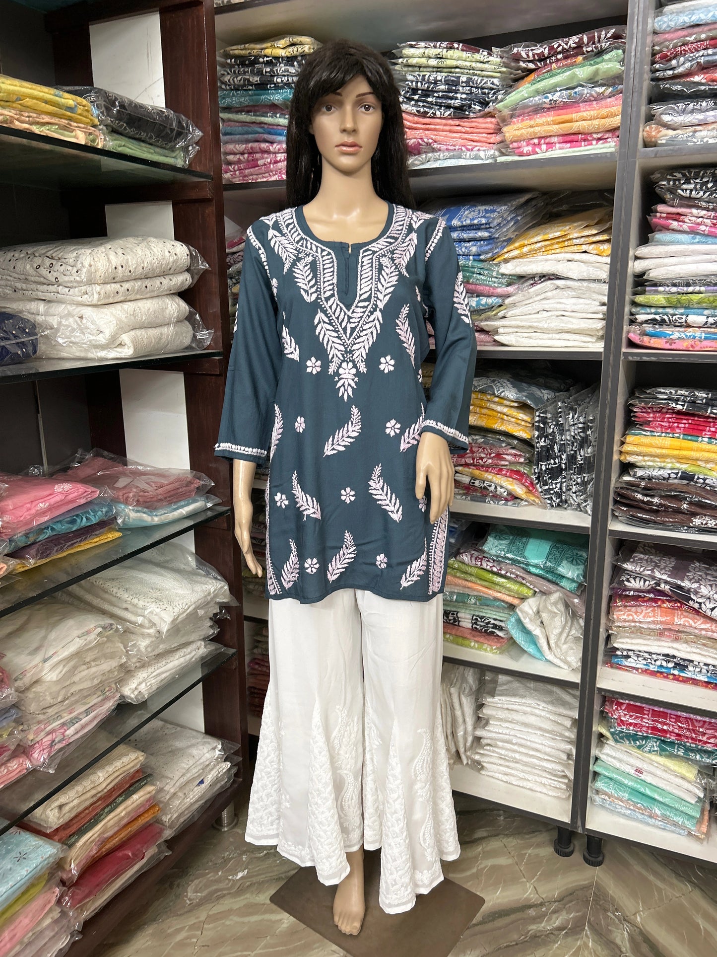 Mannequin wearing a teal embroidered top and white pants in a fabric store.