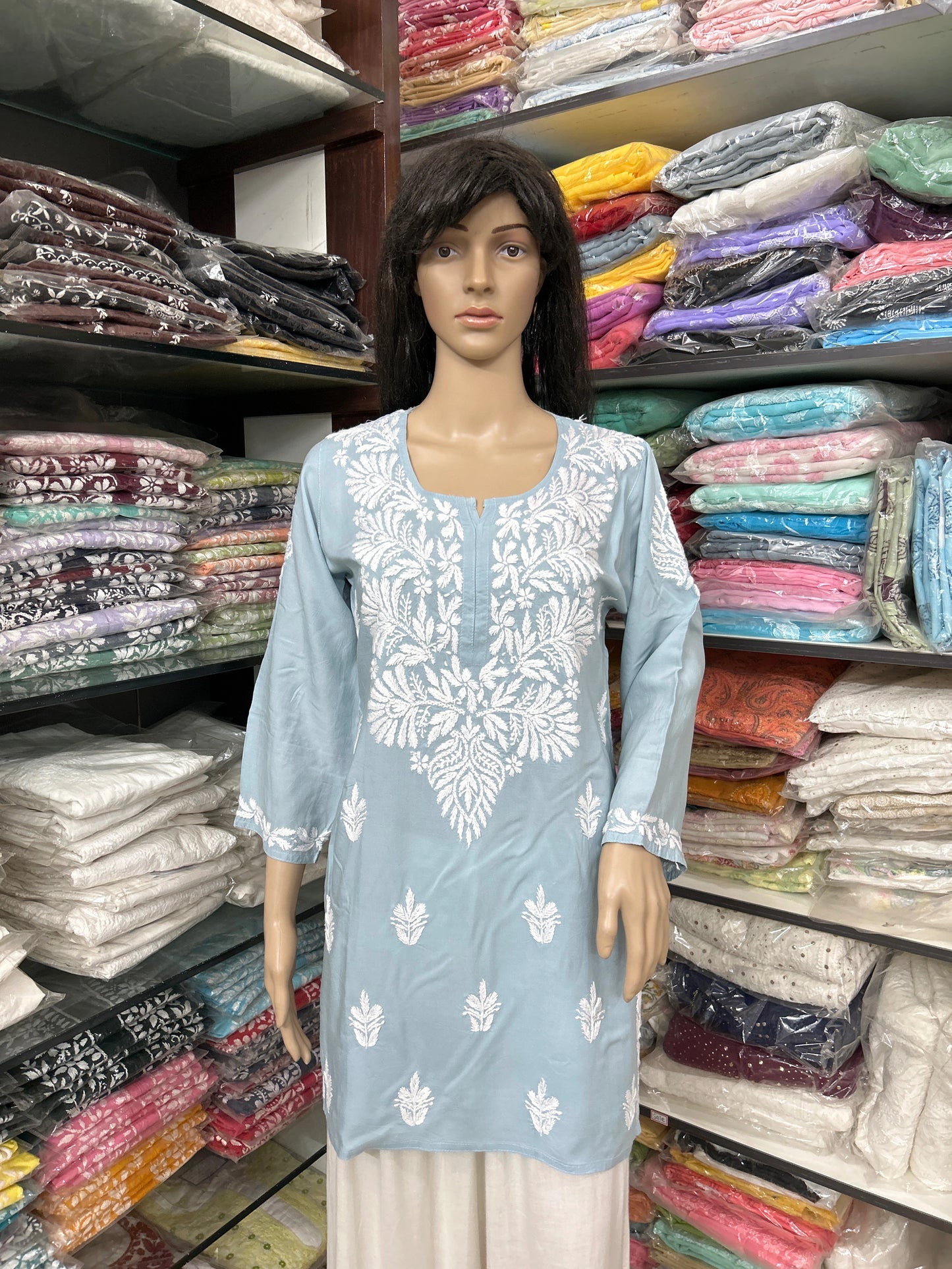 Mannequin wearing a light blue embroidered kurta with a colorful fabric background
