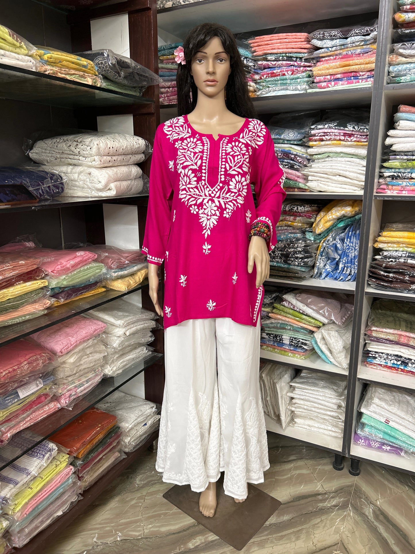 Mannequin wearing a pink embroidered top and white pants in a fabric store.
