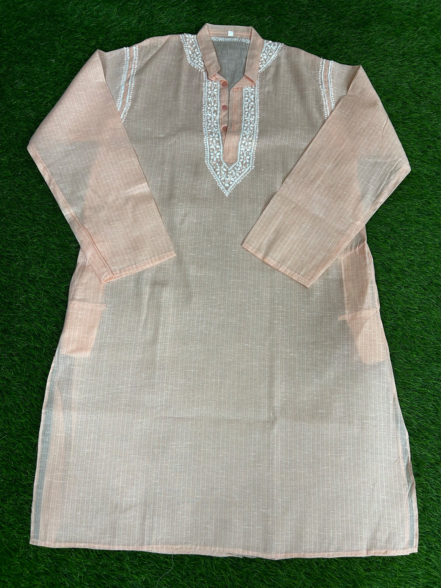 Light brown kurta with intricate white embroidery on a green background
