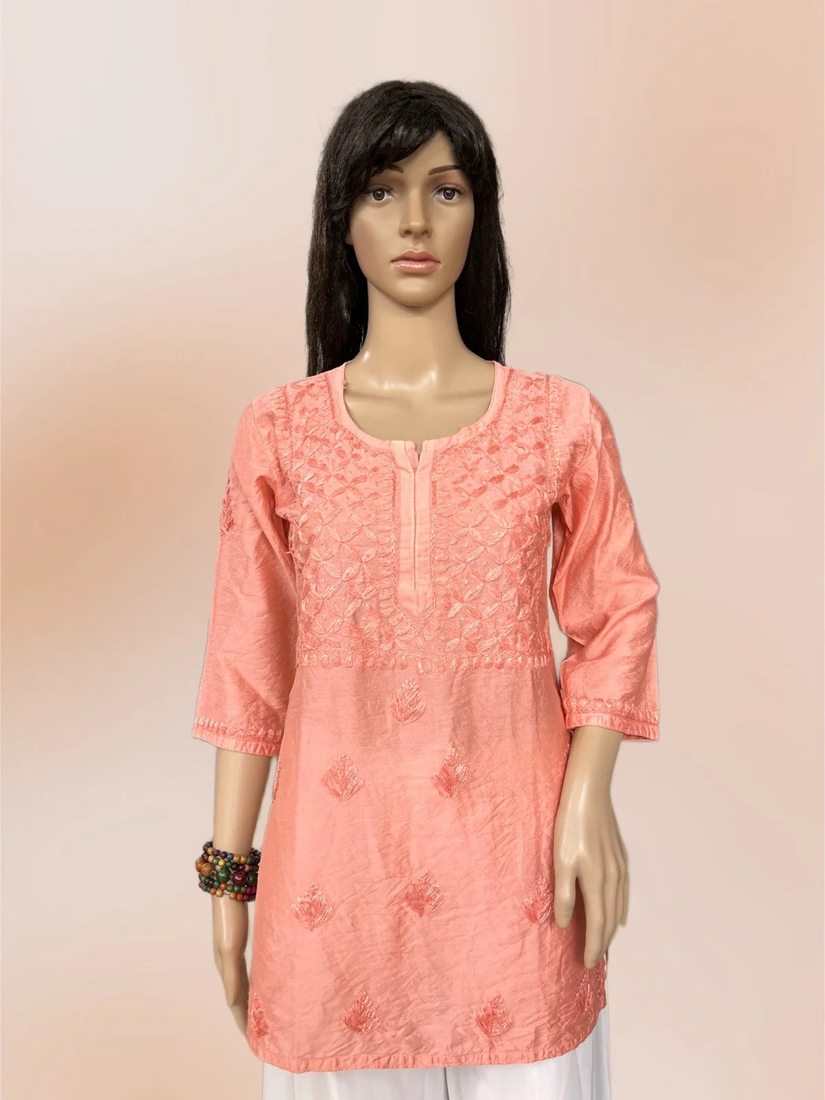Mannequin wearing a coral pink embroidered kurta with white pants on a beige background
