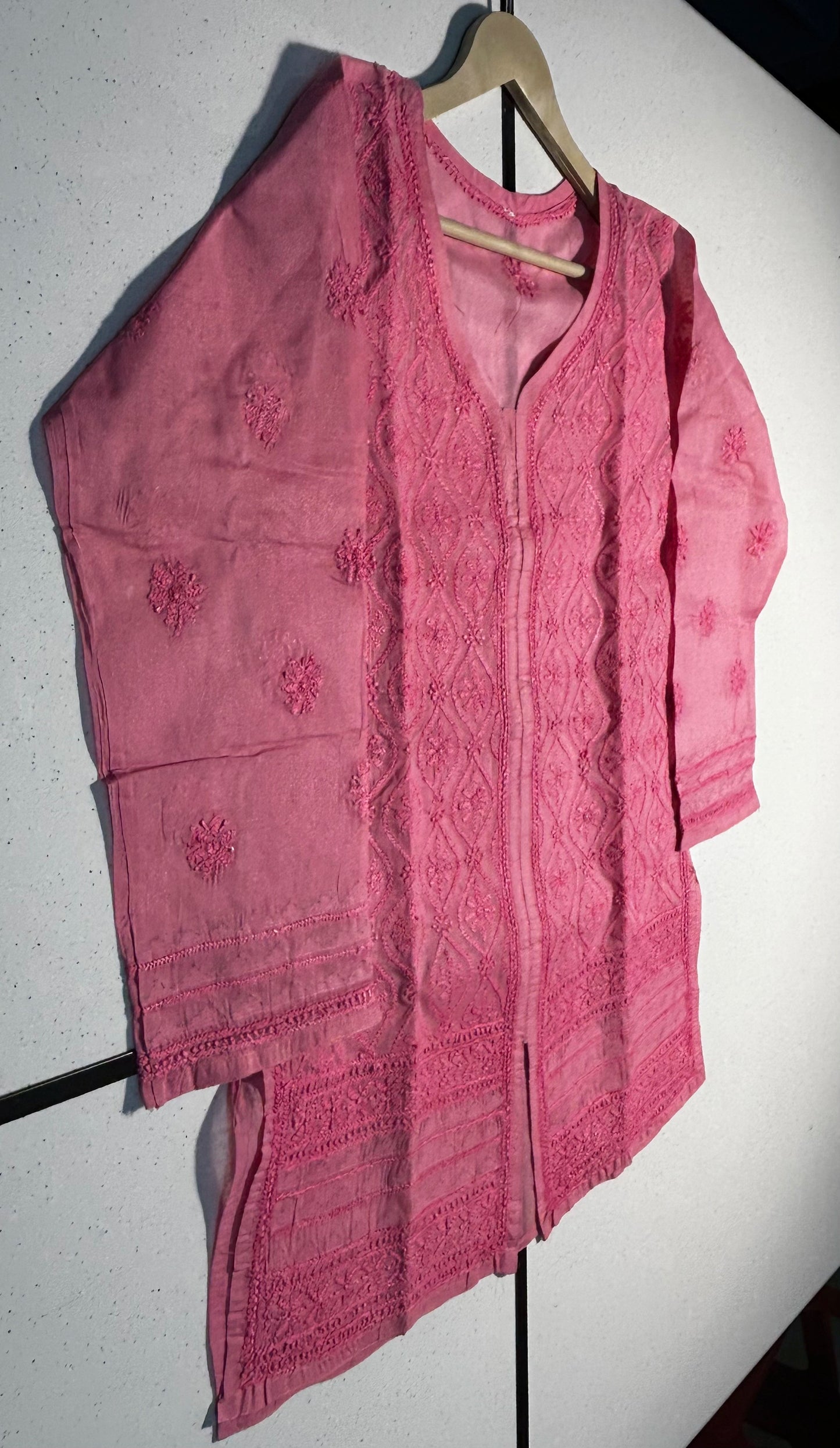 Pink embroidered shirt on a hanger against a white background