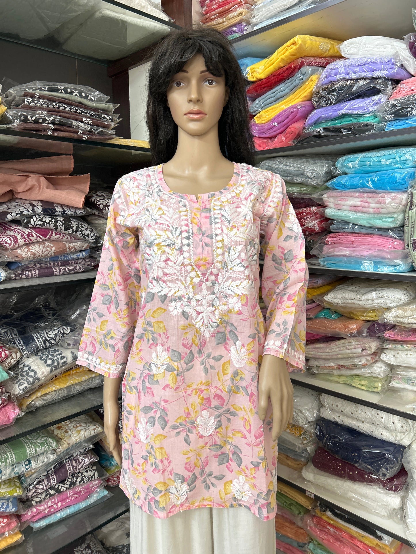lucknowi chikankari Mannequin wearing a floral pink top in a fabric store with shelves of colorful fabrics.