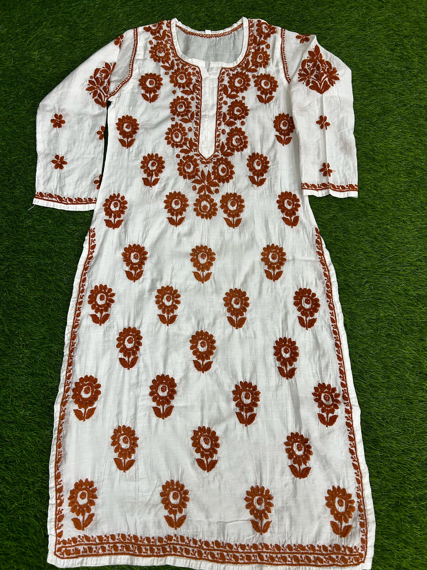 White dress with brown floral embroidery on a green background