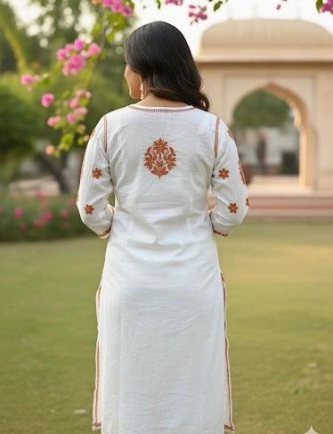 Woman wearing a white traditional outfit with orange embroidery in a garden setting