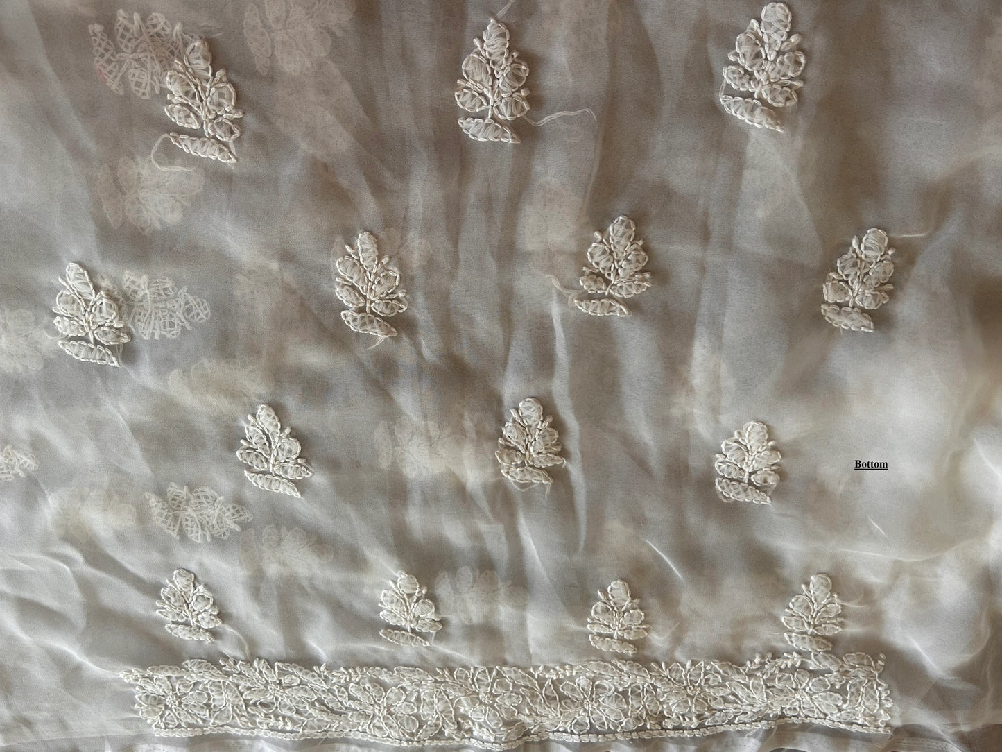 Silky fabric with intricate white floral embroidery on a light gray background