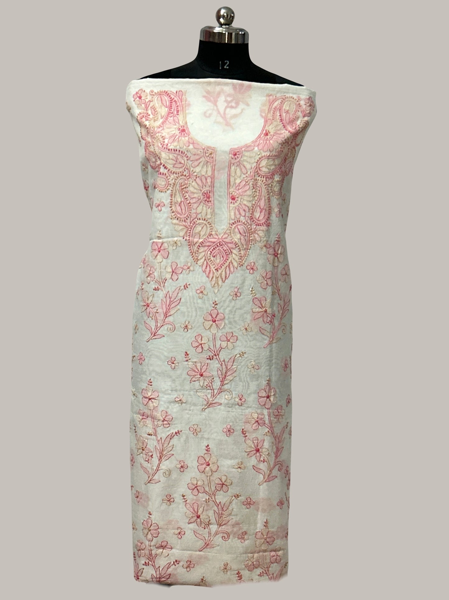 Lucknowi chikankari white dress with floral patterns on a mannequin against a gray wall with decorative panels.