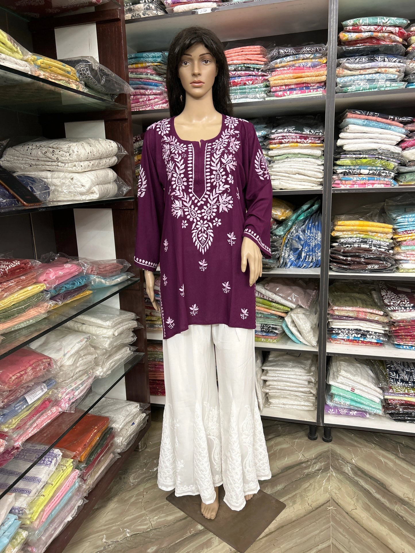 Mannequin wearing a purple embroidered top and white pants in a fabric store.