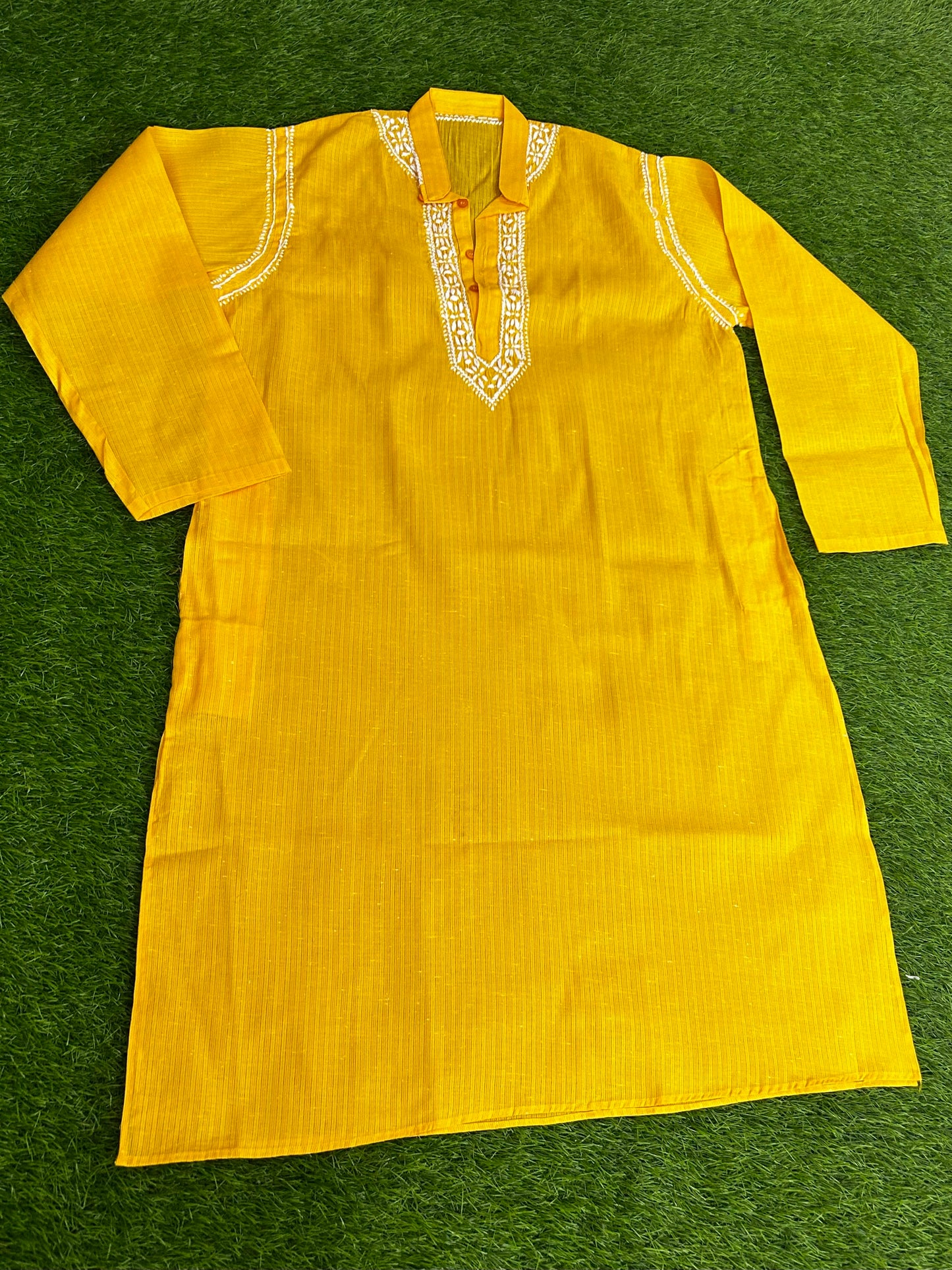 Yellow kurta with white embroidery on a green surface