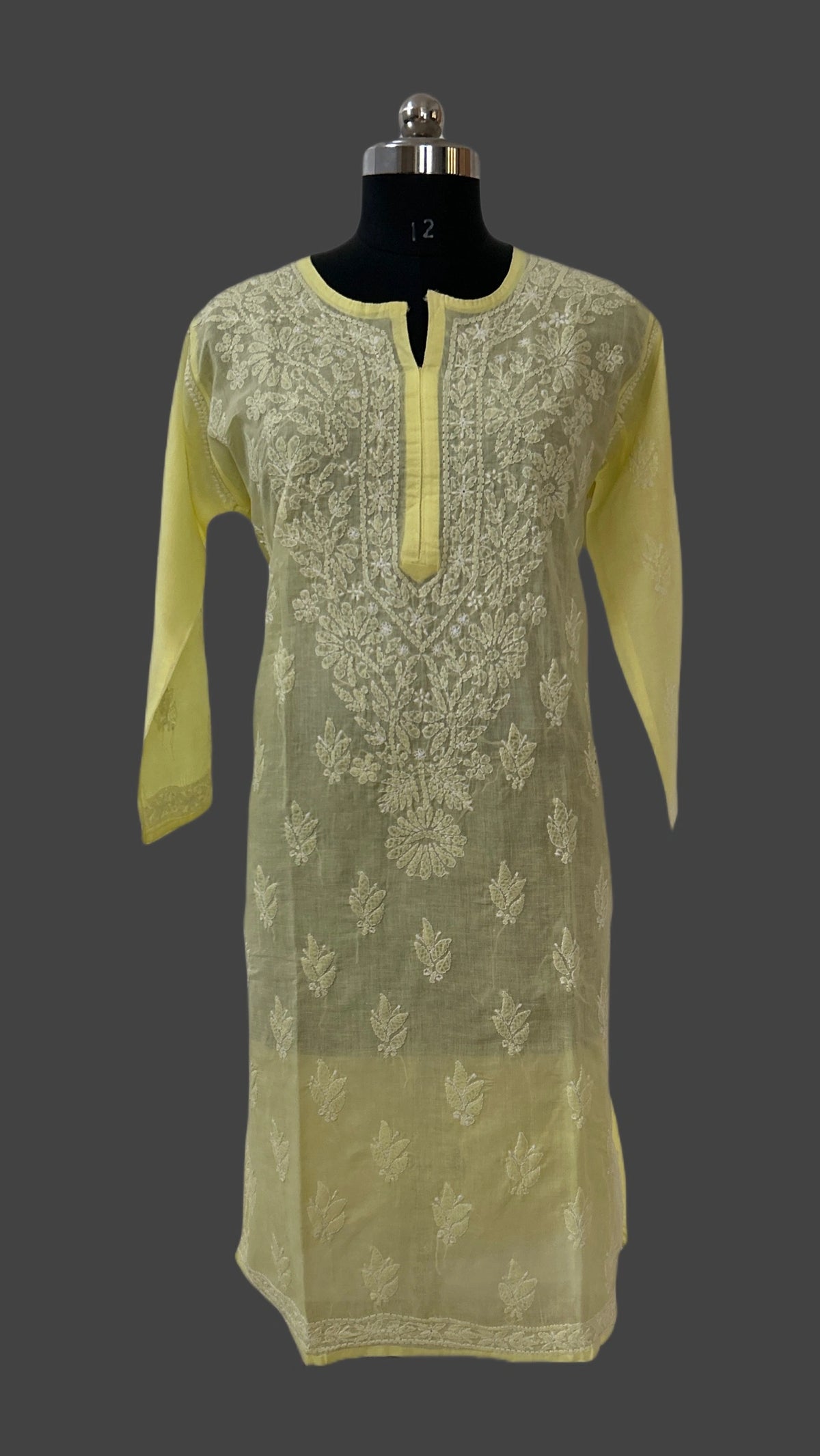 A pale yellow embroidered kurta displayed on a black dress form mannequin against a dark gray background. The kurta features a split neckline with a central keyhole cutout, a vertical yellow placket, and detailed cream embroidery on the front with matching embroidery on the sleeves.