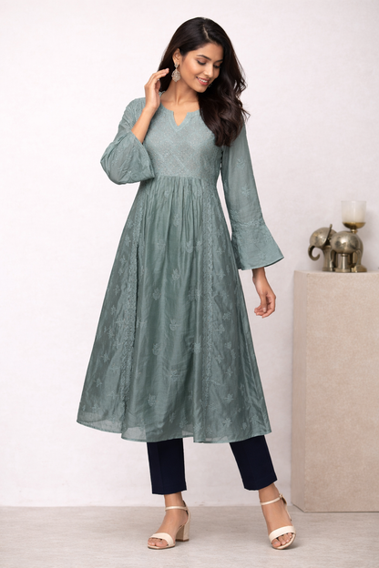 Woman wearing a green dress with long sleeves and black pants on a white background