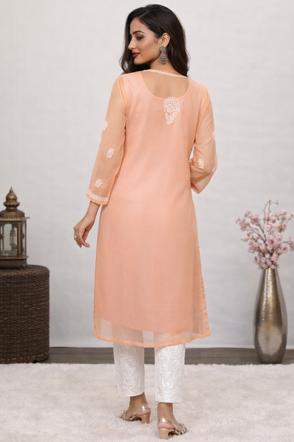 Woman wearing a peach kurta with white embroidery in a minimalistic setting.