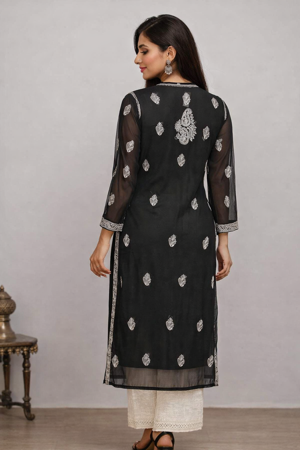 Woman wearing a black kurta with white embroidery and white pants against a gray background