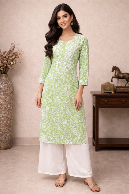 Woman wearing a light green kurta with white floral patterns and white palazzo pants, standing against a beige wall.