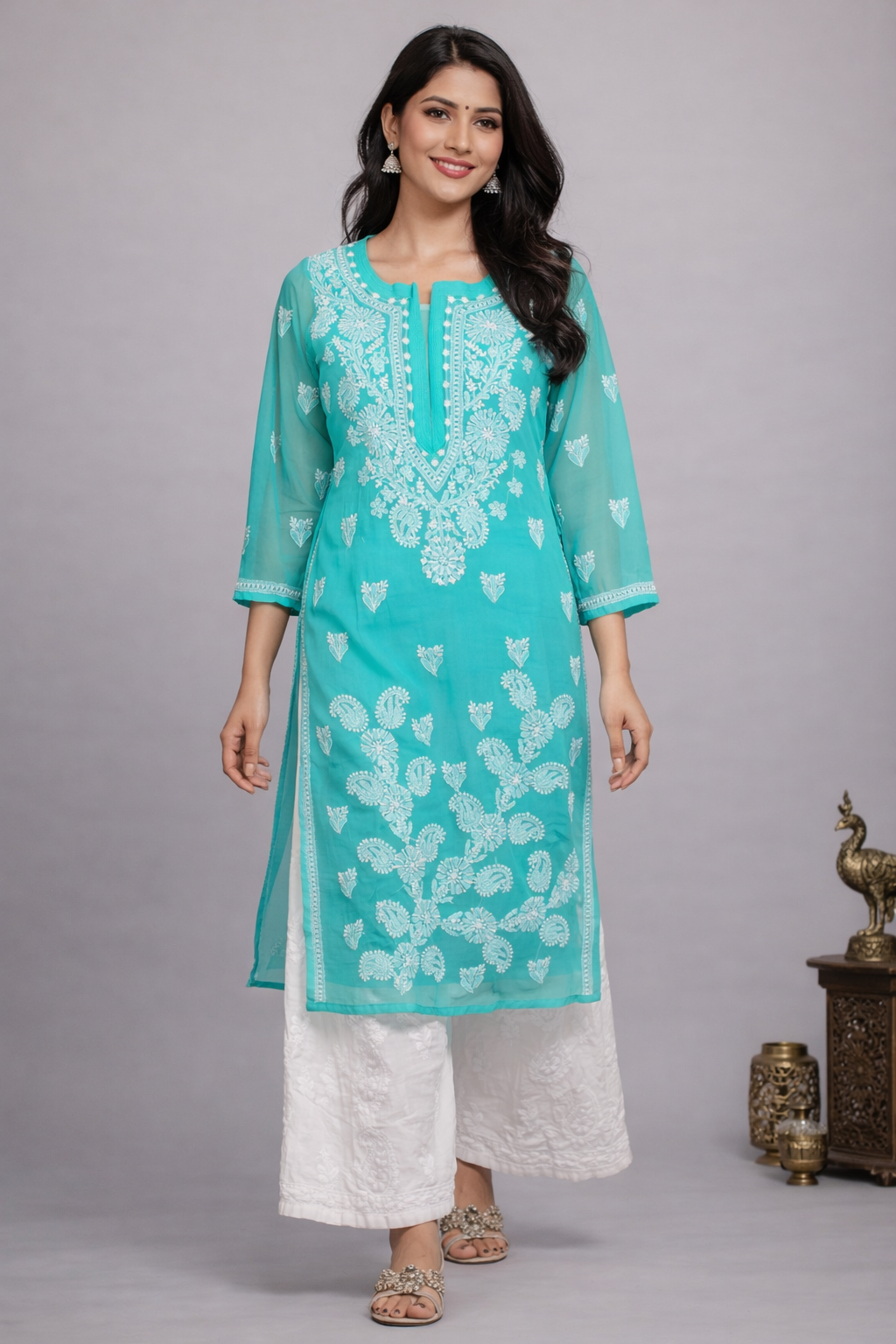 Woman wearing a turquoise embroidered kurta with white pants on a gray background