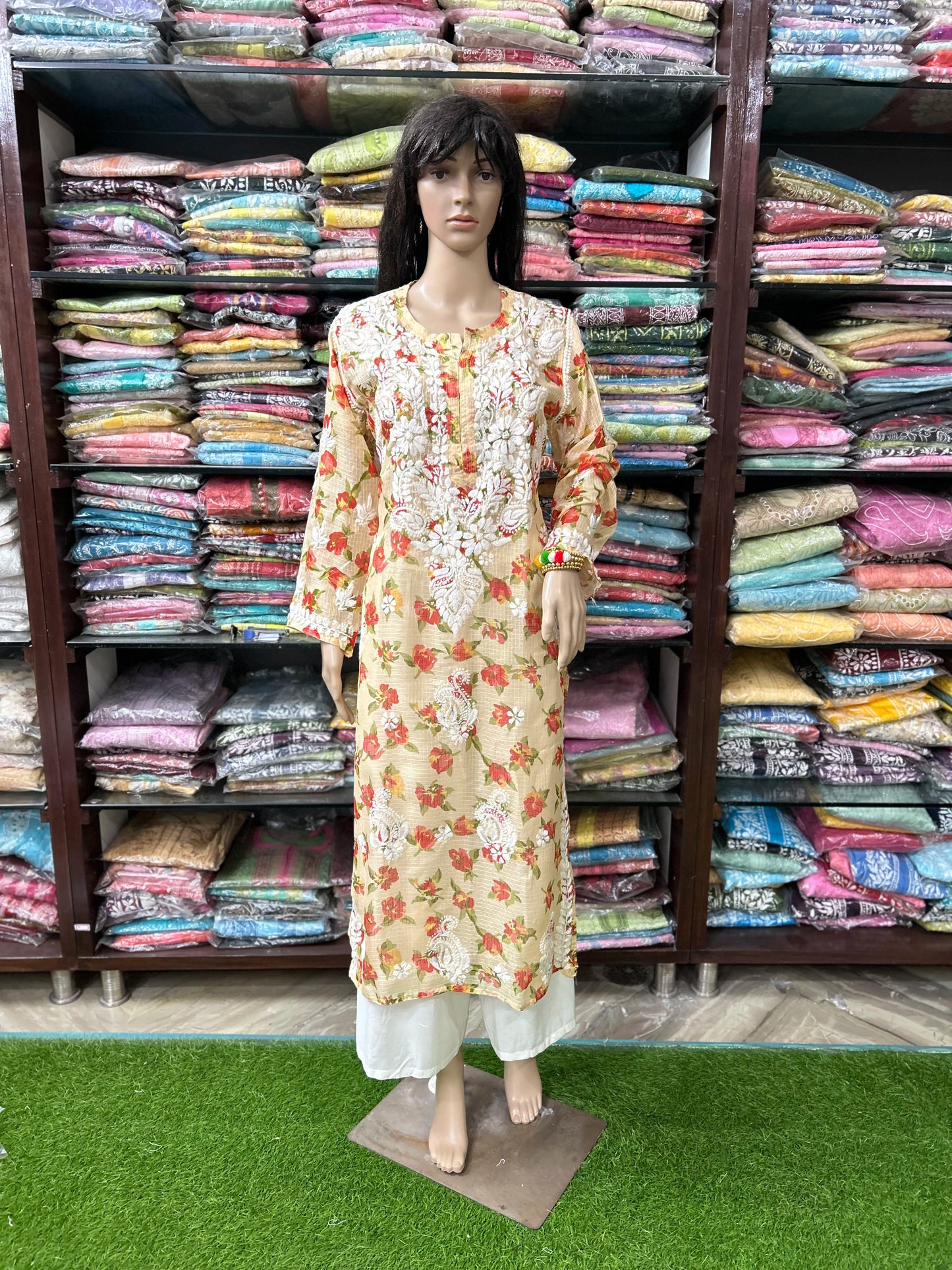 Mannequin wearing a floral dress in front of shelves filled with colorful fabrics.