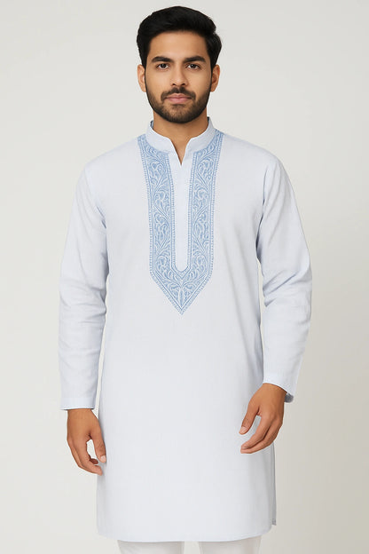 Man wearing a white kurta with blue embroidery on a light gray background