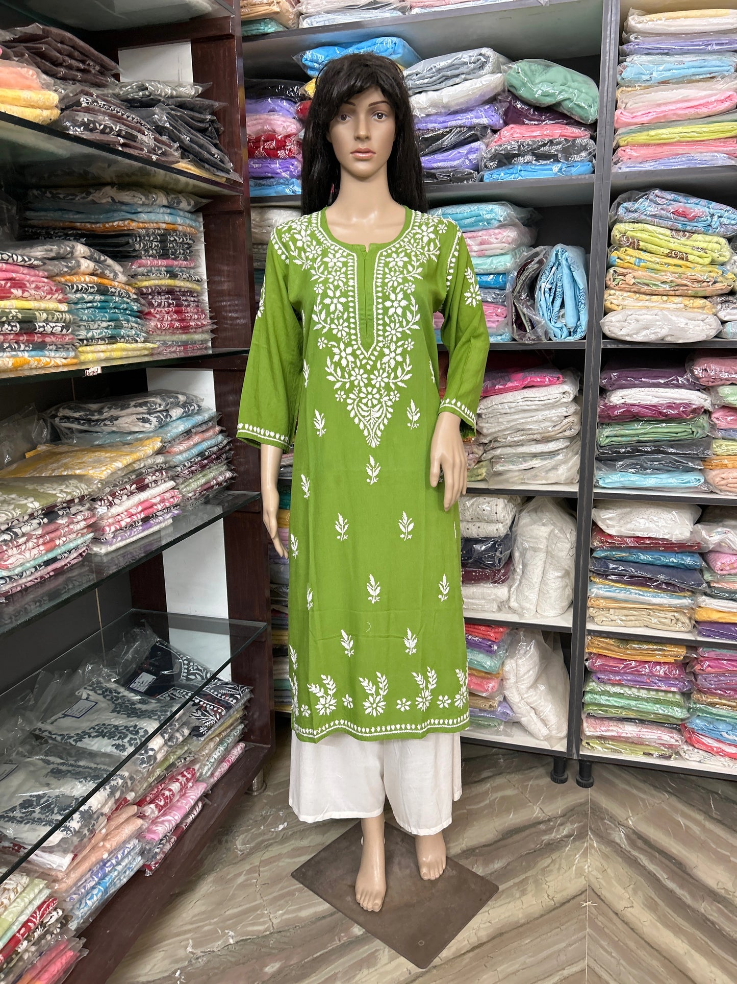 Mannequin wearing a lucknowi chikankari floral dress in a fabric store with shelves of fabric in the background.