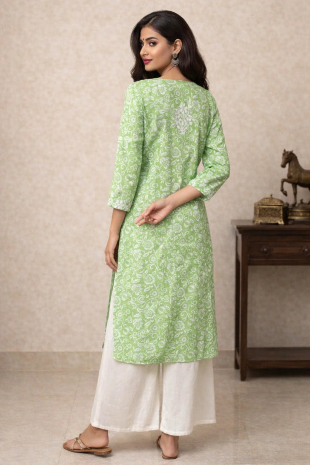 Woman wearing a green floral kurta with white pants against a beige wall.