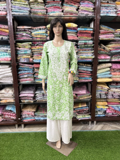 Mannequin wearing a green and white outfit in front of shelves filled with colorful fabrics.