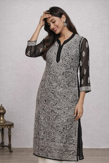 Woman wearing a black and white patterned kurta with sheer sleeves against a plain background