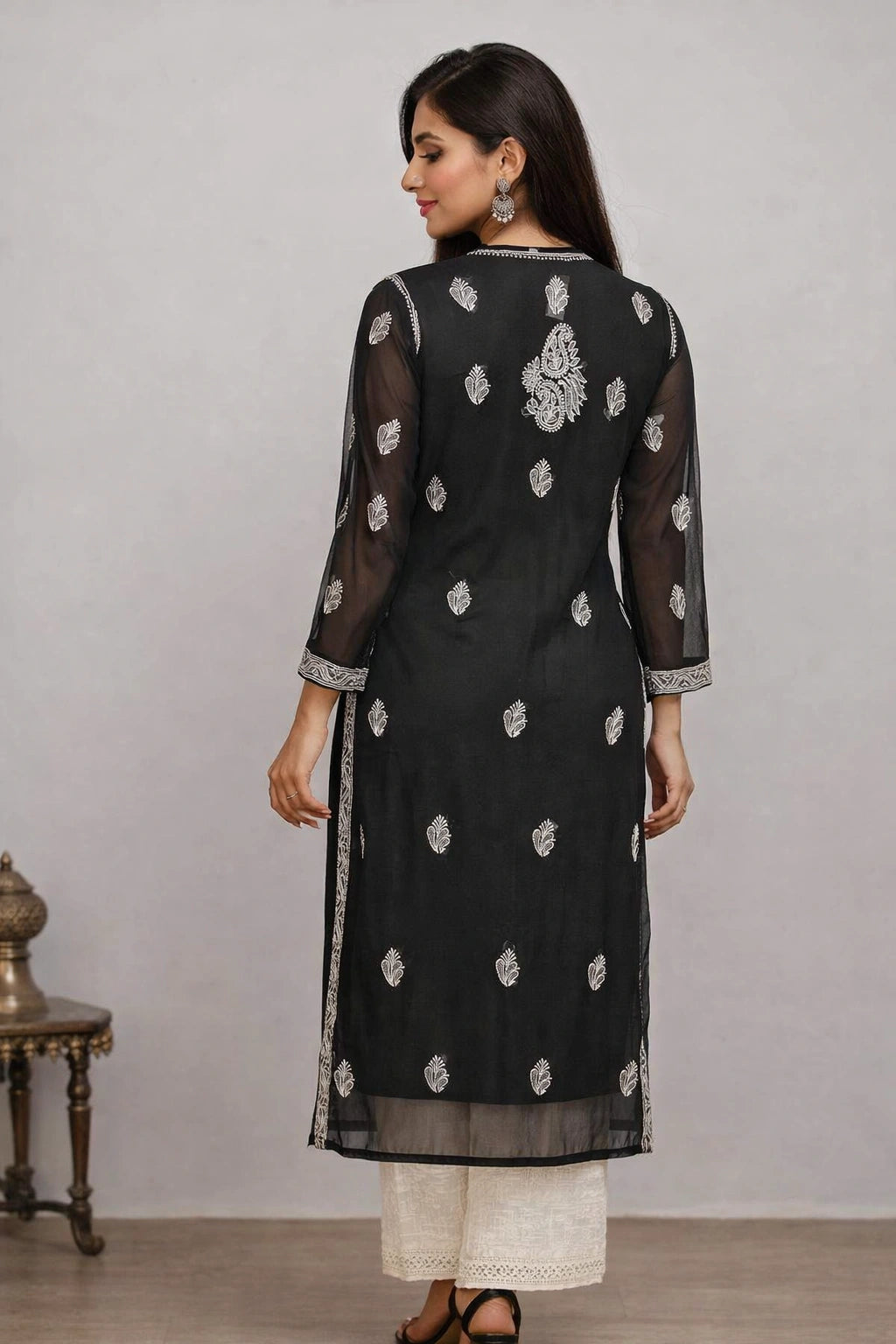 Woman wearing a black embroidered kurta with white pants against a gray background