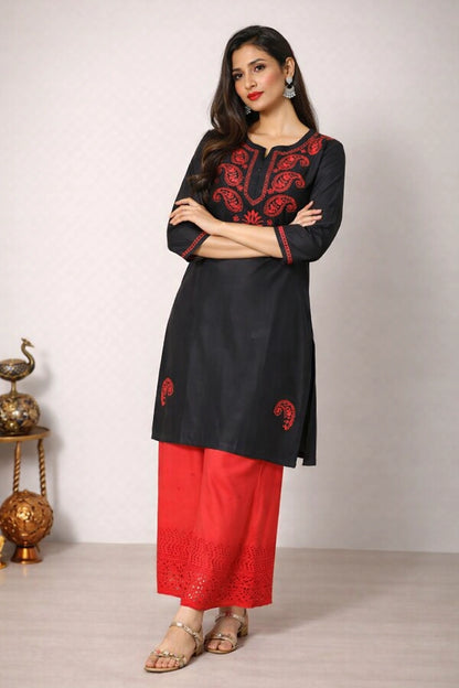 Woman wearing a black and red embroidered kurta with red pants against a white background