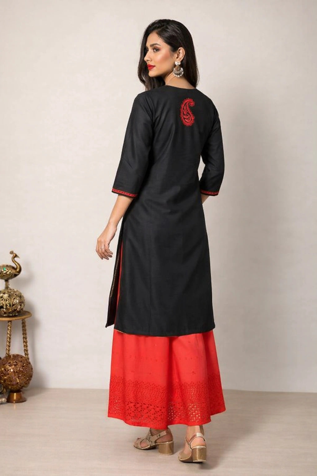 Woman wearing a black kurta with red details against a plain background