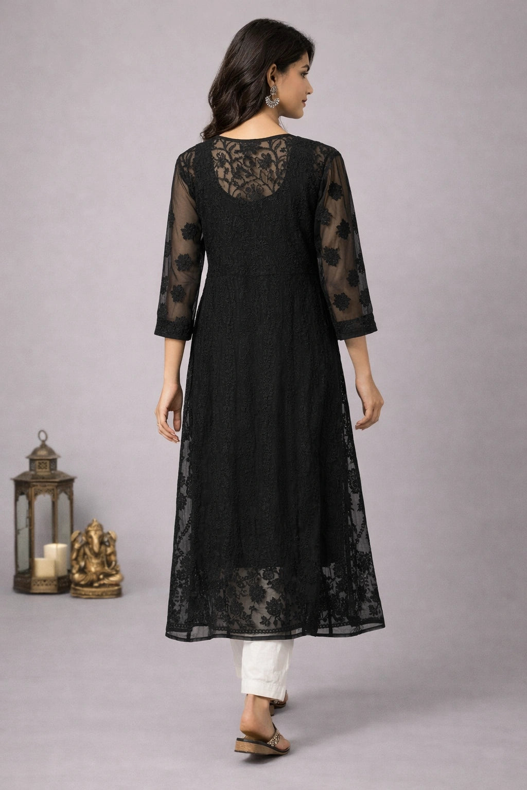 Woman wearing a black lace dress with white pants on a gray background