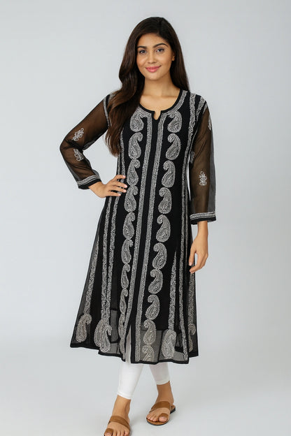 A woman modeling a black long kurta with vertical silver-gray paisley and floral embroidery, sheer black three-quarter sleeves, and white pants, standing against a light gray studio background.