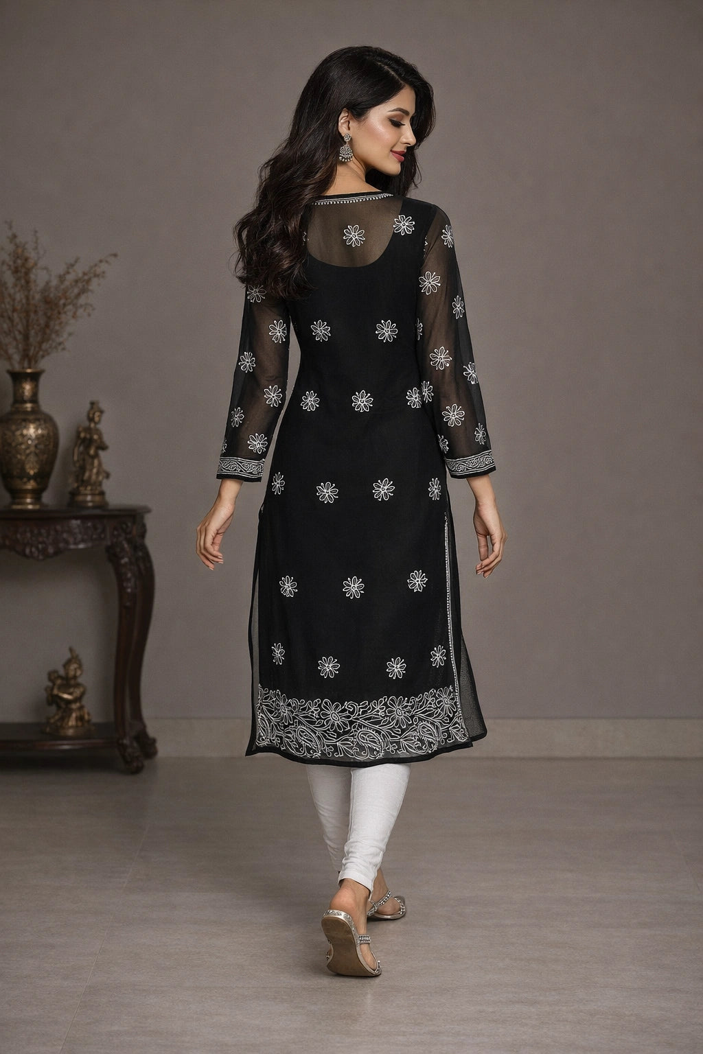 Woman wearing a black embroidered kurta with white pants in a minimalistic setting.